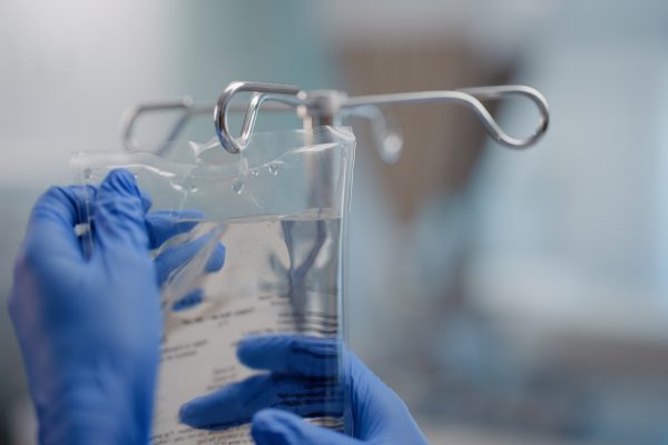 Hands, IV drip and saline solution in hospital, clinic and healthcare facility for health and healing. Doctor, nurse and closeup of medical equipment for intensive care, life support and medicine